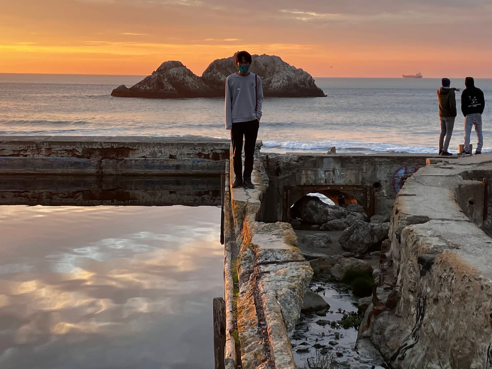 Me standing on a wall surrounded by water at Sutro Baths with the sun setting behind me.